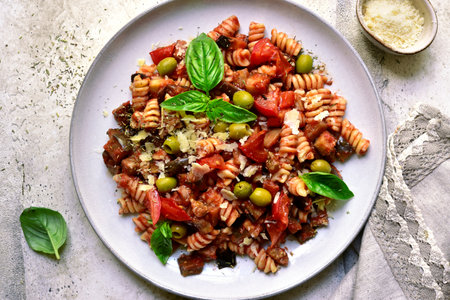 Pasta alla norma, fusilli with eggplants, tomatoes and olives on a plate over light gray slate, stone or concrete background. Traditional dish of Sicilian cuisine. Top view with copy space.の写真素材
