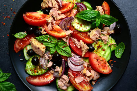 Tuna salad with cucumber and tomato on a black plate over dark slate, stone or concrete background. Top view with copy space.の写真素材