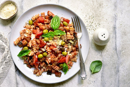 Pasta alla norma, fusilli with eggplants, tomatoes and olives on a plate over light gray slate, stone or concrete background. Traditional dish of Sicilian cuisine. Top view with copy space.の写真素材