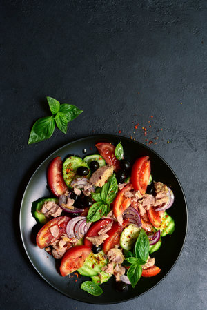 Tuna salad with cucumber and tomato on a black plate over dark slate, stone or concrete background. Top view with copy space.の写真素材