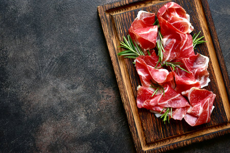 Slices of prosciutto di parma or jamon serrano (iberico) on a dark wooden background. Top view with copy space.の写真素材