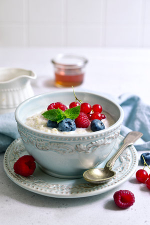 Oatmeal porridge with fresh berries and maple syrup for a breakfast in a blue bowl with spoon on a light slate, stone or concrete background.の写真素材