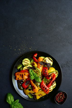 Grilled colorful vegetable: bell pepper, zucchini, eggplant on a black plate over dark slate, stone or concrete background. Top view with copy space.の写真素材