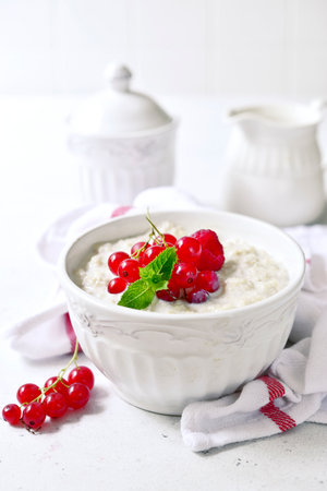 Oatmeal porridge with fresh berries and maple syrup for a breakfast in a bowl with spoon on a light slate, stone or concrete background.の写真素材