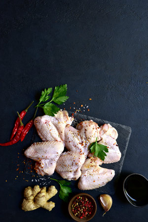 Raw chicken wings with ingredients for making on a black slate, stone or concrete background. Top view with copy space.の写真素材