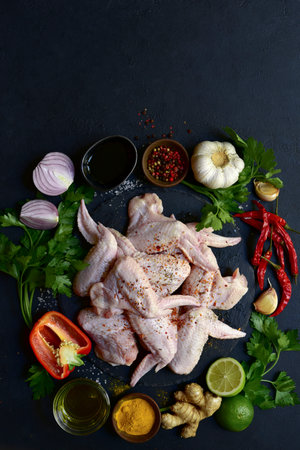 Raw chicken wings with ingredients for making on a black slate, stone or concrete background. Top view with copy space.の写真素材
