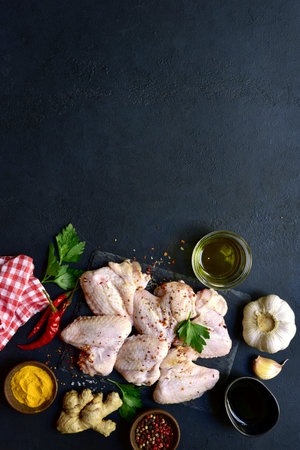 Raw chicken wings with ingredients for making on a black slate, stone or concrete background. Top view with copy space.の写真素材