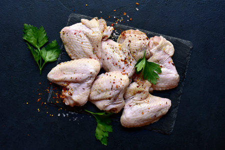 Raw chicken wings with ingredients for making on a black slate, stone or concrete background. Top view with copy space.の写真素材