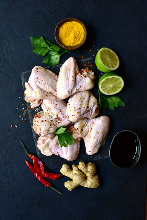 Raw chicken wings with ingredients for making on a black slate, stone or concrete background. Top view with copy space.の写真素材