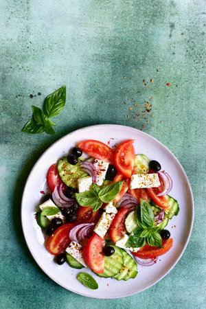 Traditional fresh vegetable Greek salad on a plate over green slate, stone or concrete background. Top view with copy space.の写真素材