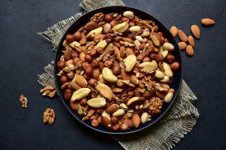 Assortment of nuts in black bowl on a dark slate, stone or concrete background. Top view with copy space.の写真素材
