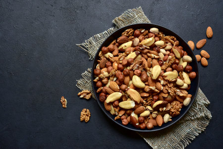 Assortment of nuts in black bowl on a dark slate, stone or concrete background. Top view with copy space.の写真素材