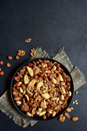 Assortment of nuts in black bowl on a dark slate, stone or concrete background. Top view with copy space.の写真素材
