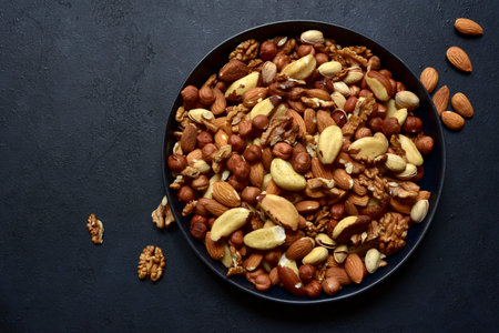 Assortment of nuts in black bowl on a dark slate, stone or concrete background. Top view with copy space.の写真素材