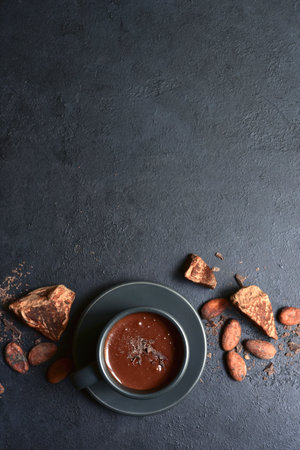 Delicious spicy hot chocolate with ingredients for making in a black cup on dark slate, stone or concrete background. Top view with copy space.の写真素材