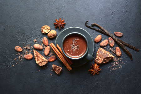 Delicious spicy hot chocolate with ingredients for making in a black cup on dark slate, stone or concrete background. Top view with copy space.の写真素材