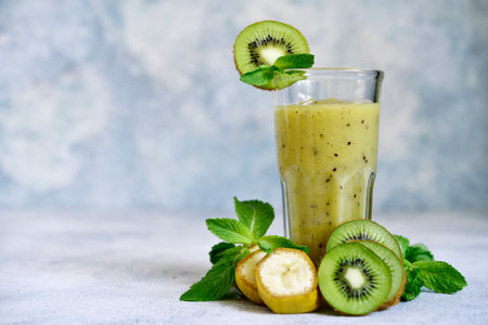 Kiwi and banana smoothie with mint in a tall glass on light blue slate, stone or concrete background.の写真素材