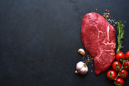 Raw organic marbled beef steak with spices and vegetables on a black slate, stone or concrete background. Top view with copy space.の写真素材