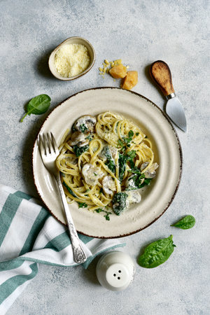 Pasta with spinach and mushrooms in a cream sauce on a light gray slate, stone or concrete background. Top view with copy space.の写真素材