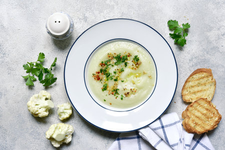 Thick cauliflower soup in a plate over light gray slate, stone or concrete background. Top view with copy space.の写真素材