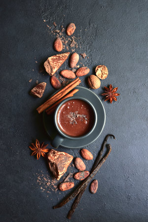 Delicious spicy hot chocolate with ingredients for making in a black cup on dark slate, stone or concrete background. Top view with copy space.の写真素材