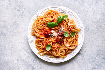 Spaghetti with grilled tomatoes on a white plate over light slate, stone or concrete background. Top view with copy space.の写真素材
