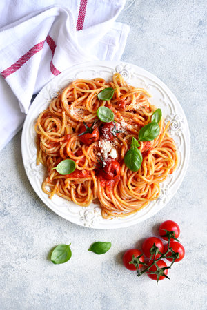Spaghetti with grilled tomatoes on a white plate over light slate, stone or concrete background. Top view with copy space.の写真素材