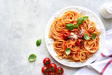 Spaghetti with grilled tomatoes on a white plate over light slate, stone or concrete background. Top view with copy space.の写真素材