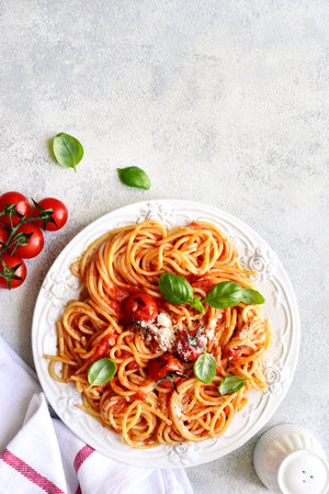 Spaghetti with grilled tomatoes on a white plate over light slate, stone or concrete background. Top view with copy space.の写真素材