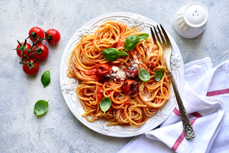 Spaghetti with grilled tomatoes on a white plate over light slate, stone or concrete background. Top view with copy space.の写真素材
