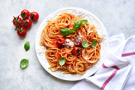 Spaghetti with grilled tomatoes on a white plate over light slate, stone or concrete background. Top view with copy space.の写真素材