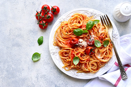 Spaghetti with grilled tomatoes on a white plate over light slate, stone or concrete background. Top view with copy space.の写真素材