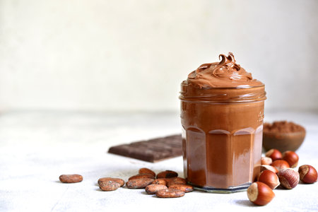 Homemade delicious chocolate and nut spread in a jar on a white slate, stone or concrete background.の写真素材