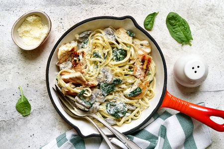 Spaghetti pasta with chicken, spinach and mushrooms in a skillet pan over light gray slate, stone or concrete background. Top view with copy space.の写真素材