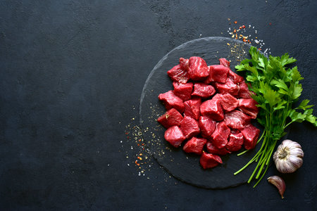 Raw organic marbled beef steak with spices and vegetables on a wooden cutting board on a black slate, stone or concrete background. Top view with copy space.の写真素材