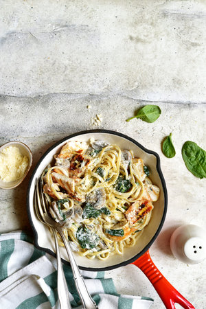 Spaghetti pasta with chicken, spinach and mushrooms in a skillet pan over light gray slate, stone or concrete background. Top view with copy space.の写真素材