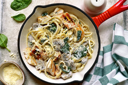 Spaghetti pasta with chicken, spinach and mushrooms in a skillet pan over light gray slate, stone or concrete background. Top view with copy space.の写真素材