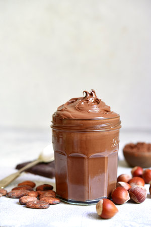 Homemade delicious chocolate and nut spread in a jar on a white slate, stone or concrete background.の写真素材