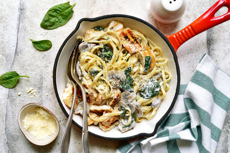 Spaghetti pasta with chicken, spinach and mushrooms in a skillet pan over light gray slate, stone or concrete background. Top view with copy space.の写真素材