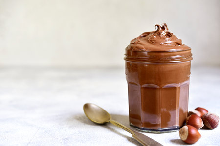 Homemade delicious chocolate and nut spread in a jar on a white slate, stone or concrete background.の写真素材