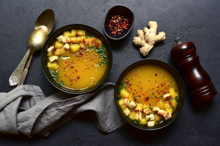 Hot spicy pumpkin soup with ginger and garlic in a black bowls over dark slate, stone or concrete background. Top view with copy space.の写真素材