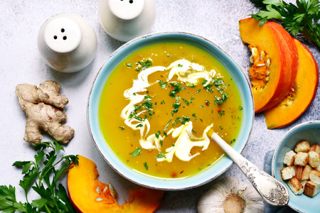 Autumn pumpkin soup with ginger and garlic in a turquoise bowl over light gray slate, stone or concrete background. Top view with copy space.の写真素材
