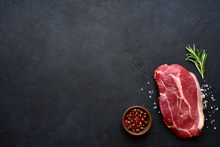 Raw organic marbled beef steak with spices on a black slate, stone or concrete background. Top view with copy space.の写真素材