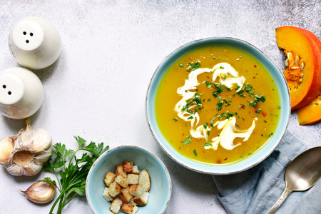 Autumn pumpkin soup with ginger and garlic in a turquoise bowl over light gray slate, stone or concrete background. Top view with copy space.の写真素材