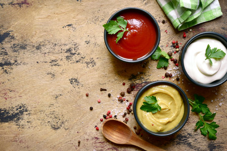 Set of popular sauces in a black bowls on a wooden slate, stone or concrete background. Top view with copy space.の写真素材