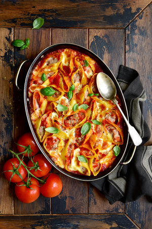 Stuffed pasta cannelloni with minced meat baked in tomato sauce in a skillet on a dark rustic wooden background. Top view with copy space.の写真素材