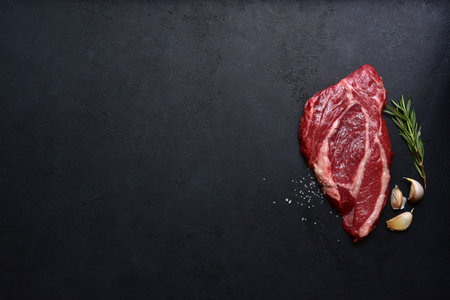 Raw organic marbled beef steak with ingredients for cooking on a black slate, stone or concrete background. Top view with copy space.の写真素材