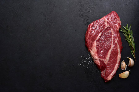Raw organic marbled beef steak with ingredients for cooking on a black slate, stone or concrete background. Top view with copy space.の写真素材