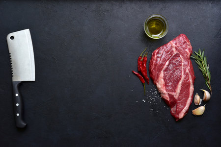 Raw organic marbled beef steak with ingredients for cooking on a black slate, stone or concrete background. Top view with copy space.の写真素材