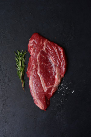 Raw organic marbled beef steak with ingredients for cooking on a black slate, stone or concrete background. Top view with copy space.の写真素材